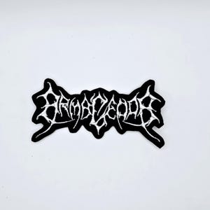 Puede incluir: Parche bordado en blanco y negro con el texto "BRAMBLECORD" en una fuente gótica. El parche tiene un fondo negro y costuras blancas, con un diseño único y estilizado. Adecuado para ropa o accesorios.