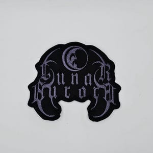 Puede incluir: Parche bordado negro con el texto "Lunar Ritual" en fuente gótica. El parche presenta un diseño de media luna en la parte superior. El parche es probablemente para ropa o accesorios.