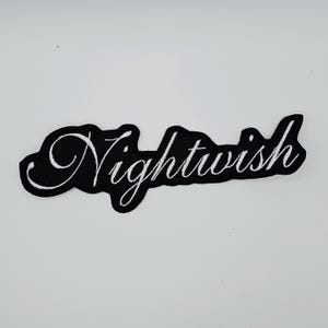 Puede incluir: Un parche negro con la palabra "Nightwish" bordada en blanco con escritura cursiva. El parche tiene un borde negro y está sobre un fondo blanco. El diseño es simple y elegante.