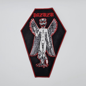 Puede incluir: Parche negro con borde rojo, con la palabra "PAZUZU" en letras góticas rojas. El parche representa un demonio alado blanco con ojos rojos y apariencia esquelética. El parche tiene forma de ataúd.