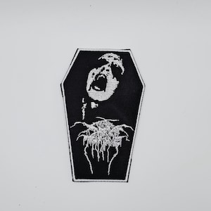 Könnte beinhalten: Schwarz-weißer, gestickter Aufnäher in Sargform. Der Aufnäher zeigt eine schreiende Figur im Sarg mit einem stilisierten, gotischen Design. Der Aufnäher ist wahrscheinlich für Kleidung oder Accessoires bestimmt.