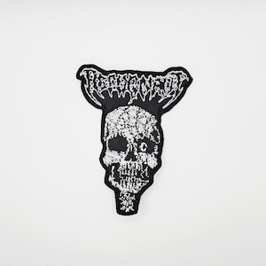 Puede incluir: Parche bordado en blanco y negro con un diseño de calavera y la palabra "RESURRECTED" en una fuente estilizada. El parche tiene un borde negro y es probablemente para ropa o accesorios.