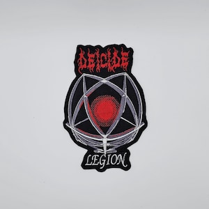 May include: Embroidered patch with the word "DEICIDE" in red, stylized lettering above a black and grey geometric design with a red centre. The word "LEGION" is below the design in white lettering.