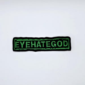 Könnte beinhalten: Ein rechteckiger Aufnäher mit dem Text "EYEHATEGOD" in Grün auf schwarzem Grund gestickt. Der Aufnäher hat einen grünen Rand und ist wahrscheinlich aus Stoff.