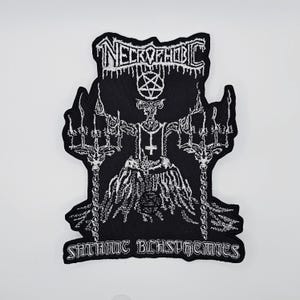May include: Black and white embroidered patch featuring the text "NECROPHOBIC" at the top and "SATANIC BLASPHEMIES" at the bottom. The patch depicts a horned figure with a pentagram and a cross, holding two candelabras.