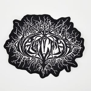 Puede incluir: Parche bordado en blanco y negro con un diseño estilizado. El parche presenta un emblema central con detalles intrincados y la palabra "EMINEM" en letras blancas en negrita. El diseño está rodeado por un borde negro con un borde dentado.