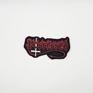 May include: Black embroidered patch with the word "Possessed" in red, gothic-style lettering. The patch features a white inverted cross and a red arrow tail design. The patch is rectangular in shape.