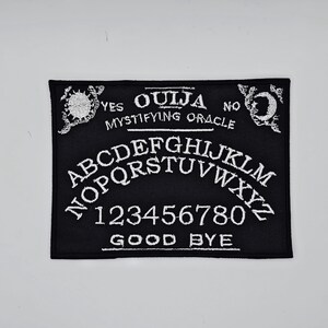 May include: Black Ouija board patch with white embroidered lettering and symbols. The patch features the alphabet, numbers, and the words "Yes," "No," "Ouija," "Mystifying Oracle," and "Good Bye."