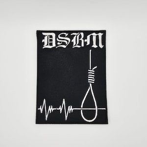 Puede incluir: Parche rectangular negro con texto bordado blanco "DSBM" en fuente gótica. Debajo, un diseño de soga blanca y una línea de latidos del corazón blanca. El parche es para ropa o accesorios.
