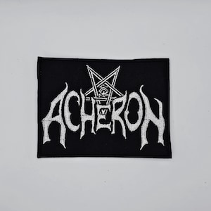 Może przedstawiać: Czarna prostokątna naszywka z białym haftowanym napisem "ACHERON" gotycką czcionką i symbolem pentagramu. Naszywka jest prawdopodobnie przeznaczona na odzież lub akcesoria, na białym tle.