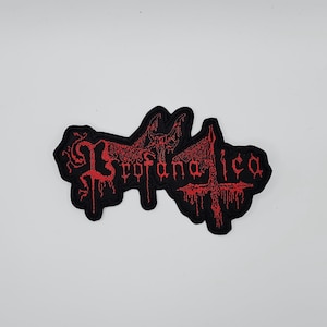 Puede incluir: Un parche bordado negro con la palabra "Profanatica" en rojo, con letras góticas. El parche presenta una criatura parecida a un murciélago y un diseño de cruz, con un efecto de goteo.
