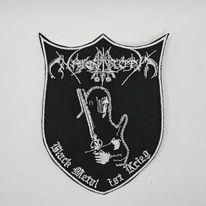 May include: Black and white embroidered patch in a shield shape. The patch features a stylized design with the text "Black Metal ist Krieg". The design includes a sword and a figure.