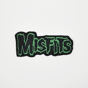 May include: Black patch with the word "MISFITS" in green, outlined in green stitching. The patch has a black background and a green, jagged border. The text is in a stylized font.