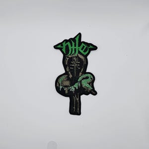 May include: Embroidered patch in black and green, depicting a hooded figure with a snake coiled around a cross. The word "nite" is in green above the figure. Suitable for clothing or accessories.