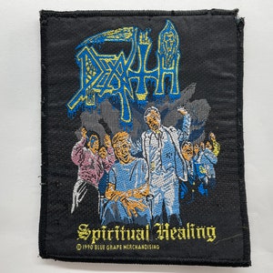 Pode incluir: Um remendo bordado preto com o nome da banda "Death" em letras amarelas e azuis. O remendo apresenta um gráfico de um grupo de pessoas em um ambiente hospitalar com o texto "Spiritual Healing" e as informações de direitos autorais "©1990 Blue Grape Merchandising".