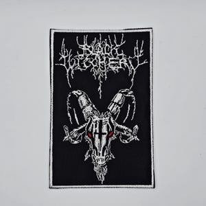 May include: Black embroidered patch featuring the text "Black Witchery" above a goat skull with red eyes. The patch is rectangular with a black background and white stitching.
