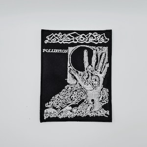 Op de afbeelding: Zwarte geborduurde patch met witte afbeelding van een hand, schedel en het woord "POLLUTION". De patch heeft het woord "Dystopia" in een gestileerd lettertype bovenaan. De patch is rechthoekig.