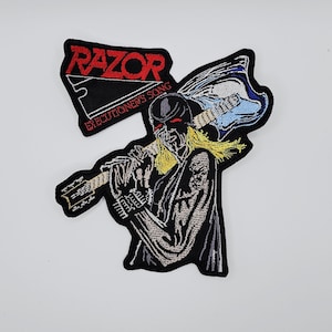May include: Embroidered patch featuring a figure with a guitar, wearing a black helmet and cape. The patch has the word "RAZOR" in red and the text "EXECUTIONER'S SONG". The guitar is blue and white.