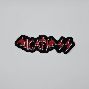 May include: A black embroidered patch with the word "DEATH" in a stylized font. The letters are red with white accents, and the patch has a black border. The design includes lightning bolt symbols.