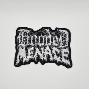 Può includere: Una toppa ricamata in bianco e nero con la scritta "THUNDER MANIFEST". La toppa ha un bordo nero e il testo è in un carattere gotico. Il design è dettagliato e intricato.