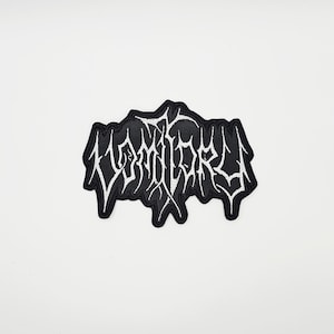 Könnte beinhalten: Schwarz-weißer, gestickter Aufnäher mit dem Wort "VOMITORY" in einer stilisierten, gotischen Schrift. Der Aufnäher hat einen schwarzen Hintergrund mit weißen Nähten für den Text und den Rand. Geeignet für Kleidung oder Accessoires.