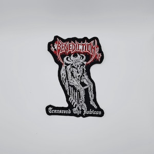 Puede incluir: Parche bordado en blanco y negro con la palabra "Benediction" en letras góticas rojas. Presenta una detallada ilustración blanca de una figura con cuernos. El texto "Transcend The Rubicon" está debajo.