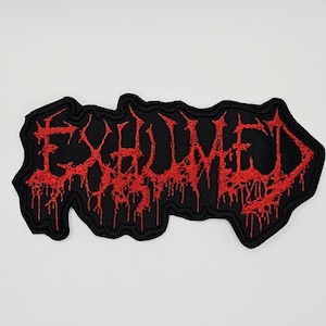 May include: A black embroidered patch featuring the word EXHUMED in a stylized, dripping red font. The lettering has a jagged, distressed appearance with thin lines extending downward to mimic a melting or bleeding effect against the black fabric.