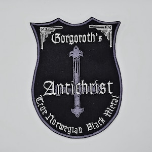 May include: Black patch with a shield shape and a gray border. The patch features the text "Gorgoroth's Antichrist True Norwegian Black Metal" in white, with a gray cross design in the center.