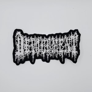 May include: Black and white embroidered patch with the word "DECOMPOSED" in a gothic font. The patch has a jagged border and is likely for clothing or accessories. The text is in white, and the patch itself is black.