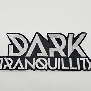 Könnte beinhalten: Ein schwarz-weiß gestickter Aufnäher mit dem Schriftzug "DARK TRANQUILLITY" in einer stilisierten Schriftart. Der Text ist in weißem Garn auf schwarzem Hintergrund mit schwarzem Rand.