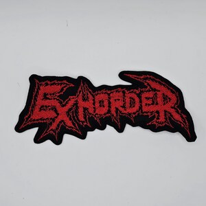 Op de afbeelding: Zwart geborduurde patch met het woord "EXHORDER" in rode, gekartelde letters. De patch heeft een zwarte rand en is bedoeld voor kleding of accessoires.