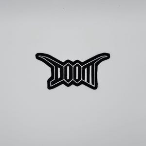 May include: Black and white embroidered patch with the word "DOOM" in a stylized font. The patch has a unique, angular design and is set against a white background. The patch is likely for clothing or accessories.
