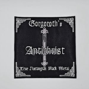 May include: Black square patch with white embroidered text and a silver inverted cross. The patch reads "Gorgoroth's Antichrist" with "True Norwegian Black Metal" below. The border has a decorative white design.