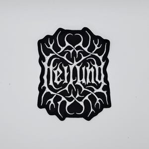 Op de afbeelding: Een zwart-wit geborduurde patch met het woord "Fellund" in gotische letters. De patch heeft een uniek, sierlijk ontwerp met een zwarte achtergrond en witte details. De patch is waarschijnlijk voor kleding of accessoires.