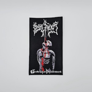 Peut inclure: Écusson rectangulaire noir avec texte blanc et un dessin d'une figure avec du sang rouge. Le texte en haut dit "Dying Fetus" dans une police gothique. Le texte en bas dit "Grotesque Impalement".