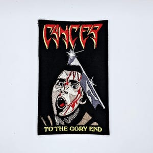 May include: Embroidered patch with the word "CANCER" in red and yellow, above a graphic illustration of a person with a bloody face and a blade. The text "TO THE GORY END" is at the bottom.