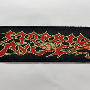 以下が含まれることがあります： 中央に五芒星が描かれた「MORBID ANGEL」という赤い刺繍と緑色の刺繍のロゴが施された黒い織りパッチ。右下に「© 1991 MORBID ANGEL」の文字があります。