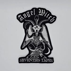 Könnte beinhalten: Schwarz-weißer, gestickter Aufnäher mit einer gehörnten Figur, Flügeln und einer Flamme. Der Aufnäher trägt die Aufschrift "Angel Witch" und "Seventies Tapes". Das Design beinhaltet Halbmonde. Geeignet für Kleidung oder Accessoires.