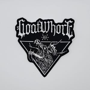 Puede incluir: Parche bordado en blanco y negro con el nombre de la banda "Goatwhore" en letras góticas sobre una ilustración detallada de una figura demoníaca dentro de un triángulo blanco. El parche tiene un borde negro.