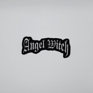 Può includere: Toppa ricamata nera con la scritta "Angel Witch" in lettere gotiche bianche. La toppa ha un bordo nero ed è progettata per essere cucita o stirata su abiti o accessori. Sfondo bianco.