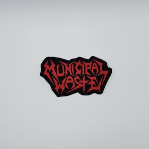 Puede incluir: Un parche negro con la inscripción roja "MUNICIPAL WASTE" en una fuente gótica estilizada. El parche tiene una forma irregular. Está diseñado para ser cosido o planchado en ropa o accesorios. El tema está relacionado con la música.