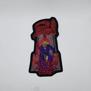 May include: Embroidered patch with a black border featuring the word "DEATH" in red gothic lettering above an illustration of a robed figure holding a golden chalice. The text "SCREAM BLOODY GORE" is below the figure in red.