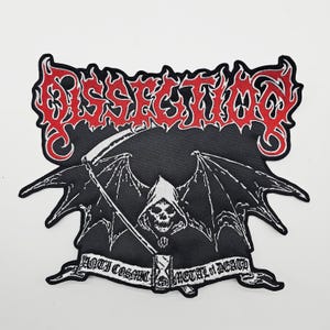 以下が含まれることがあります： 鎌を持った死神とコウモリの羽が描かれた白黒のパッチ。「DISSECTION」の文字が炎のような赤い文字で描かれています。下のバナーには「ANTI COSMIC METAL OF DEATH」と書かれています。