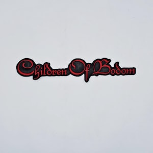 以下が含まれることがあります： 黒と赤のパッチ。テキスト「Children of Bodom」が様式化されたフォントで表示されています。テキストは赤で縁取られ、内部は黒です。パッチはおそらくジャケットやバッグ用です。