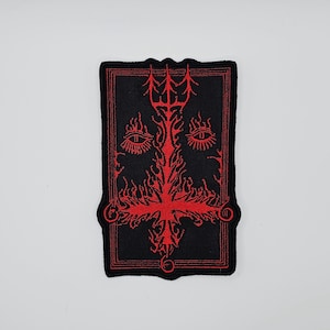 May include: Black rectangular patch with a red inverted cross design. The patch features a red border and a detailed illustration of a trident, eyes, and flames. The design is centered on the patch.