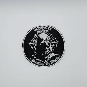 Peut inclure: Écusson brodé noir et blanc avec les mots "Ghoulnatics Asylum" et "Metallicus Ex Mortis" dans un design circulaire. Il présente une figure de goule et une toile d'araignée.