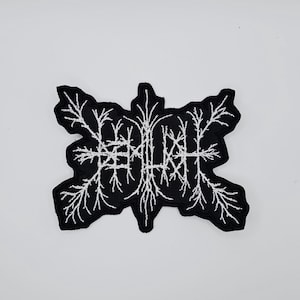 Op de afbeelding: Zwart geborduurde patch met een wit, gestileerd ontwerp dat lijkt op een netwerk van takken of wortels. De patch heeft een unieke, onregelmatige vorm en is waarschijnlijk bedoeld om op kleding of accessoires te worden genaaid.