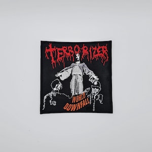 May include: Black square patch with the word "TERRORIZER" in red, stylized, gothic lettering. Below, a white illustration depicts a figure with outstretched arms, flanked by two figures, with the words "WORLD DOWNFALL" in orange.