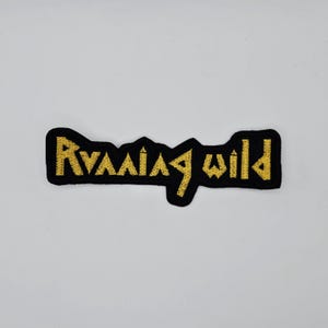 May include: A black embroidered patch with the words "Running Wild" in gold thread. The text is in a stylized font, and the patch has a black border. The patch is rectangular in shape.