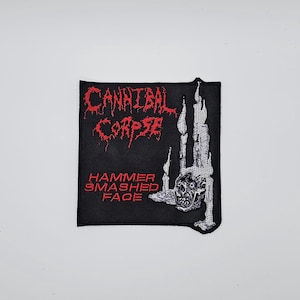 May include: Black square patch with the words "CANNIBAL CORPSE" in red, stylized lettering. Below, in red, is "HAMMER SMASHED FACE." A detailed, grayscale illustration of a skull and flames is on the right.